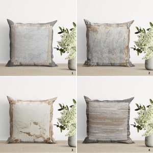 Op de afbeelding: Vier decoratieve kussens met verschillende patronen. De kussens zijn allemaal rechthoekig en hebben een witte achtergrond met een grijs, bruin of beige patroon. De kussens zijn gerangschikt in een rasterpatroon op een houten oppervlak.