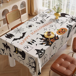 May include: White tablecloth with a Halloween theme featuring black bats, spiders, ghosts, a haunted house, a pumpkin, and the text "Happy Halloween!"