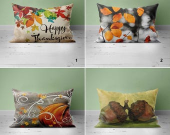 May include: Four different pillow designs featuring autumnal themes. The first pillow has a beige background with colorful fall leaves and the text "Happy Thanksgiving". The second pillow has a black and white background with orange leaves. The third pillow has a gray background with a pumpkin and swirling leaves. The fourth pillow has a beige background with two acorns.
