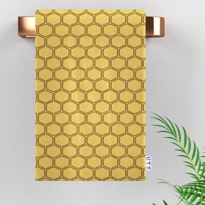 May include: A gold honeycomb patterned bath towel hanging on a towel rack. The towel has a white border and the text "UTT" is printed on the bottom right corner.