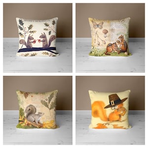 May include: Four decorative throw pillows with a nature theme. The pillows feature illustrations of squirrels, mushrooms, butterflies, and leaves. The pillows are all beige with brown and green accents. The pillows are arranged in a grid pattern on a white wooden surface.