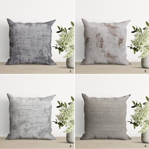 Op de afbeelding: Vier verschillende decoratieve kussens met verschillende abstracte patronen in grijstinten, bruin en wit. De kussens zijn gerangschikt in een raster op een houten oppervlak.