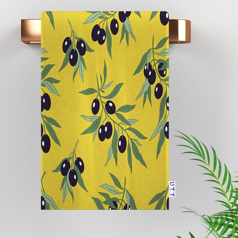 A yellow kitchen towel with a repeating pattern of black olives and green olive branches.
