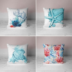 Pode incluir: Quatro almofadas brancas com desenhos em aquarela. Os desenhos incluem corais, uma estrela do mar, uma concha com estrelas do mar e um padrão de recife de coral. As almofadas têm cores azul, vermelha e branca.