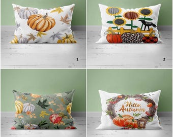 May include: Four different throw pillow designs featuring autumn themes. The first pillow has a white background with orange and white pumpkins and yellow leaves. The second pillow has a white background with sunflowers, a black bird, and pumpkins. The third pillow has a green background with orange and white pumpkins, leaves, and small pumpkins. The fourth pillow has a white background with a wreath of branches, berries, and leaves with the text "Hello, Autumn" and two orange pumpkins.
