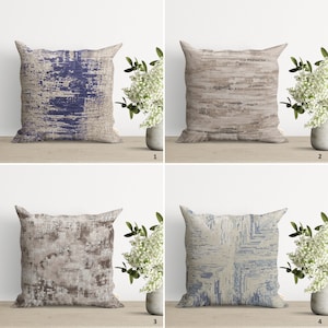 Op de afbeelding: Vier decoratieve kussens met abstracte patronen in tinten blauw, bruin en beige. De kussens zijn gerangschikt in een rasterpatroon op een houten oppervlak.