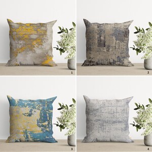 Op de afbeelding: Vier decoratieve kussens met abstracte patronen in grijstinten, blauw en geel. De kussens zijn gerangschikt in een raster op een houten oppervlak.