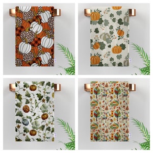 May include: Four different kitchen towels with various patterns. The first towel features a pumpkin and leaf pattern in orange, brown, and white. The second towel has a green leaf and pumpkin pattern in orange, green, and white. The third towel has a green leaf and pumpkin pattern in orange, green, and white. The fourth towel has a colorful pattern of trees, animals, and geometric shapes.