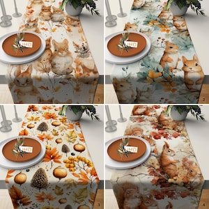 May include: Four different table runners with a fall theme. Each runner features a different design with squirrels, leaves, and acorns. The runners are all white with brown, orange, and yellow accents.