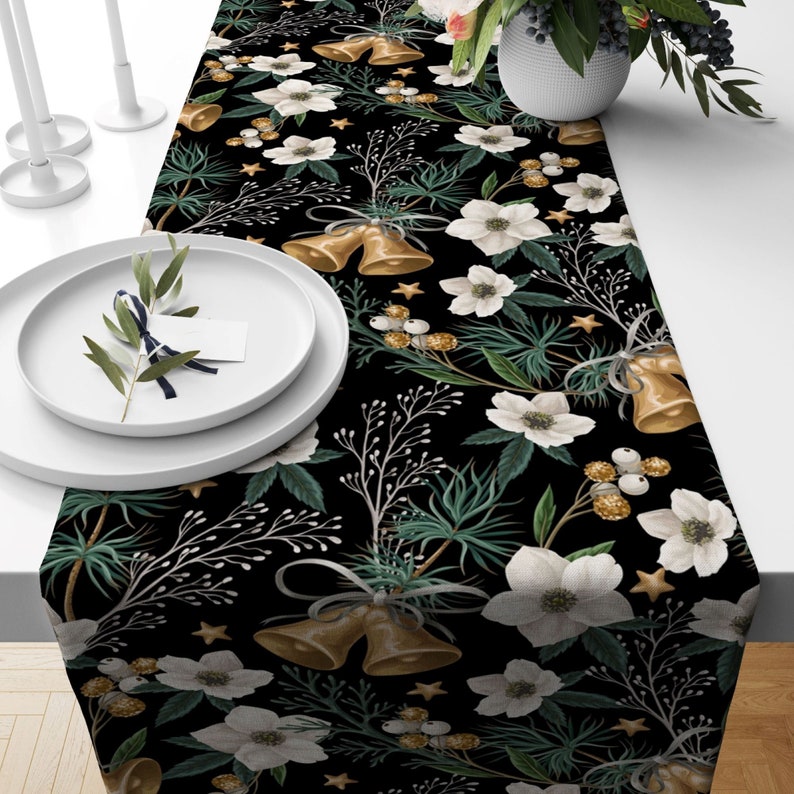 Black table runner with a repeating pattern of white flowers, gold bells, and green leaves.