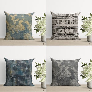 Op de afbeelding: Vier verschillende kussens met geometrische patronen. De kussens liggen op een houten oppervlak met een witte muur op de achtergrond. De kussens zijn in verschillende kleuren, waaronder zwart, wit, grijs, blauw en geel.