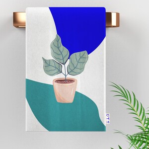 May include: A white towel with a blue, green, and white abstract design. A potted plant with green leaves is in the center of the towel. The text "UTT" is in the bottom right corner of the towel.