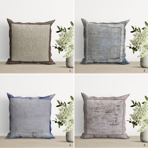 Op de afbeelding: Vier decoratieve kussens met verschillende patronen. De kussens zijn allemaal vierkant en hebben een kleurenschema in bruin, blauw, grijs en roze. De kussens zijn gerangschikt in een rasterpatroon op een houten oppervlak.