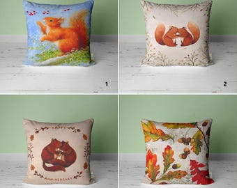May include: Four different pillow designs featuring watercolor illustrations of squirrels and autumn leaves. The first pillow has a blue background with a squirrel reaching for berries. The second pillow has a beige background with two squirrels cuddling. The third pillow has a beige background with two squirrels cuddling and the text "Happy Anniversary". The fourth pillow has a beige background with a pattern of autumn leaves and acorns.