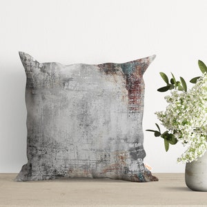 May include: A square throw pillow with a gray, white, and brown abstract design. The pillow has a distressed, textured look.