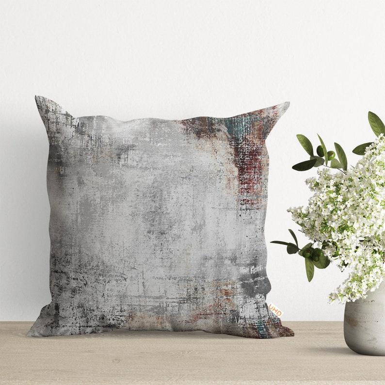 May include: A square throw pillow with a gray, white, and brown abstract design. The pillow has a distressed, textured look.