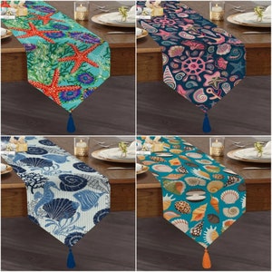 May include: Four table runners with different nautical themed designs. The first runner features red starfish on a turquoise background. The second runner has a navy blue background with pink and white seashells, anchors, and a ship's wheel. The third runner has a blue and white striped background with blue seashells, coral, and fish. The fourth runner has a turquoise background with brown and white seashells.