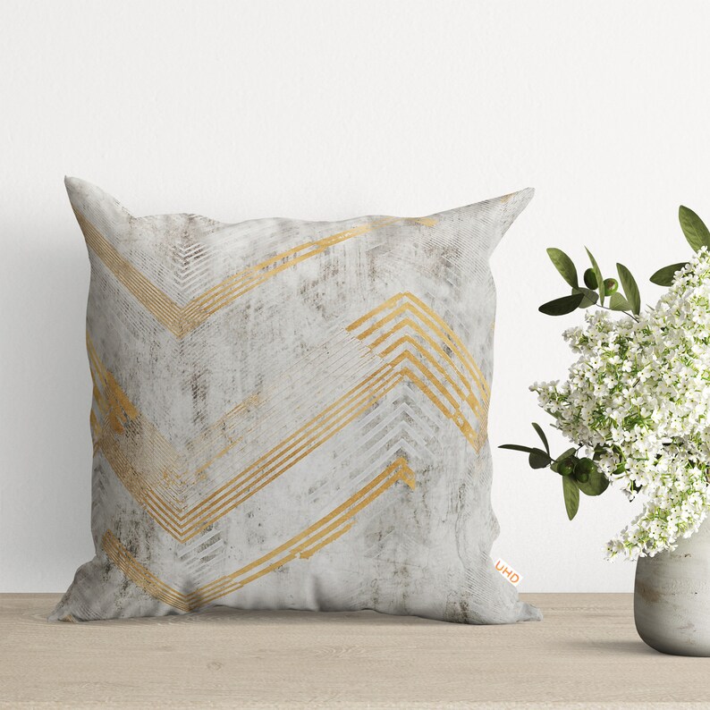 May include: A white and gold decorative pillow with a chevron pattern. The pillow has a subtle distressed look and the gold chevron pattern is slightly raised.