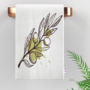 A white kitchen towel with a brown and green olive branch illustration. The branch has leaves and olives. The towel has a green and brown watercolor splatter pattern.