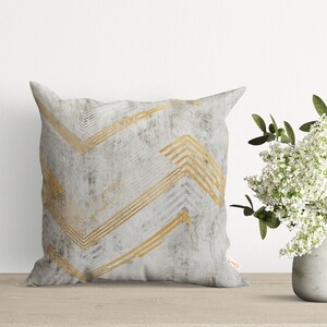 May include: A white and gold decorative pillow with a chevron pattern. The pillow has a subtle distressed look and the gold chevron pattern is slightly raised.