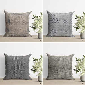 Op de afbeelding: Vier decoratieve kussens met verschillende geometrische patronen. De kussens zijn allemaal vierkant en hebben een neutrale kleurenpalet van beige, grijs en zwart.