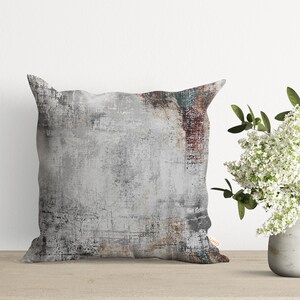 May include: A square throw pillow with a gray, white, and brown abstract design. The pillow has a distressed, textured look.
