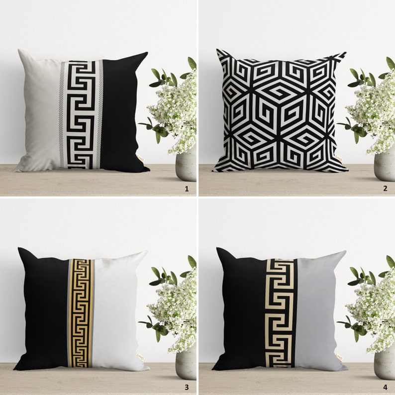 Four decorative throw pillows with black and white geometric patterns and gold Greek key trim.