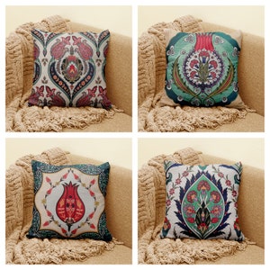 May include: Four decorative throw pillows with a floral pattern. The pillows are on a light brown couch with a fringe trim. The pillows are all different designs, but they all have a similar color scheme of red, green, and blue.
