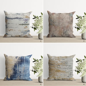 Op de afbeelding: Vier decoratieve kussens met abstracte patronen in tinten blauw, bruin, geel en grijs. De kussens zijn gerangschikt in een rasterpatroon op een houten oppervlak.