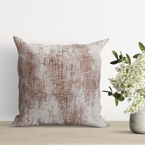 May include: A square throw pillow with a white and brown abstract pattern. The pillow has a distressed look with a subtle grid pattern.