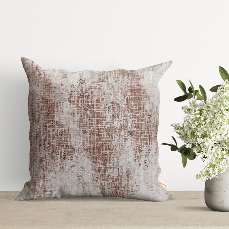 May include: A square throw pillow with a white and brown abstract pattern. The pillow has a distressed look with a subtle grid pattern.