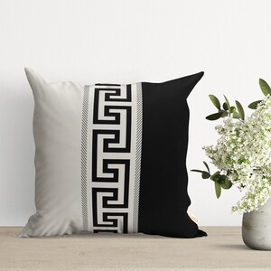 A white and black decorative pillow with a Greek key pattern border.