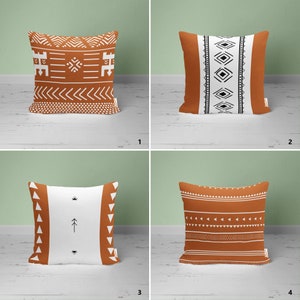May include: Four different throw pillow designs with geometric patterns in white, black, and brown on a rust-colored background. The pillows are arranged in a grid pattern on a white surface.