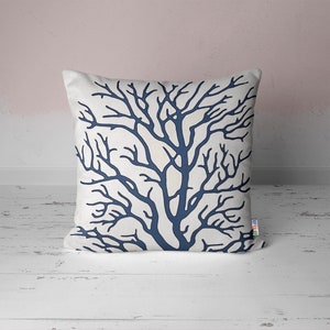 A white throw pillow with a navy blue coral branch design.