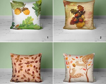 May include: Four different throw pillow designs featuring autumnal themes. The first pillow has a white background with green leaves and yellow acorns. The second pillow has a brown background with green leaves and brown acorns. The third pillow has a brown background with a repeating pattern of brown acorns and leaves. The fourth pillow has a white background with a brown tree with two squirrels and the text "Give Thanks".