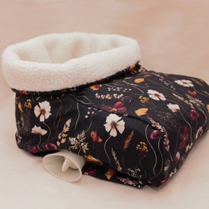 Può includere: Una fodera per borraccia dell'acqua calda in tessuto con stampa floreale bianco e nero con fodera in sherpa bianca. La fodera ha un beccuccio in plastica bianca.