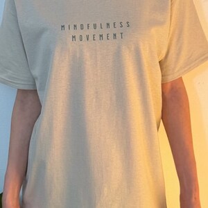 May include: A light beige t-shirt with the text "MINDFULNESS MOVEMENT" printed on the front.