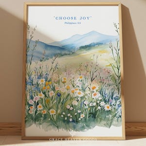 May include: Watercolor print in a wooden frame featuring a serene landscape with mountains and wildflowers. The artwork includes the text "CHOOSE JOY" and "Philippians 4:4" in blue. The painting showcases a field of colorful flowers.