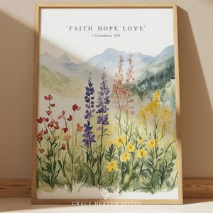May include: Watercolor print in a wooden frame featuring a field of wildflowers in shades of red, purple, and yellow, with a mountain backdrop. The text "FAITH HOPE LOVE" and "1 Corinthians 13:13" are at the top.