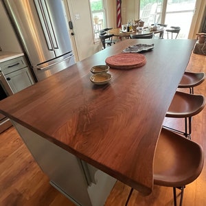 May include: A light blue kitchen island with a dark wood countertop and a live edge. The island has two brown leather bar stools with black metal frames. There are two small bowls on the countertop.