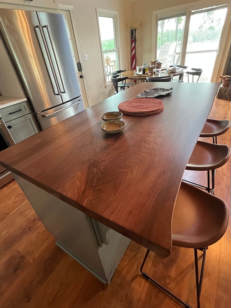 May include: A light blue kitchen island with a dark wood countertop and a live edge. The island has two brown leather bar stools with black metal frames. There are two small bowls on the countertop.