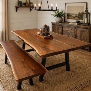May include: A rectangular dining table and a matching bench, both featuring natural live-edge wood surfaces with a rich brown finish. The furniture pieces are supported by sturdy, black metal legs, showcasing a combination of organic wood grain.