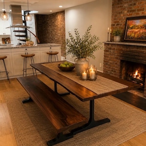 May include: A rectangular live-edge wood dining table with a dark brown finish and black metal T-shaped legs. The table is paired with a matching long wooden bench and features a textured tan table runner, a grey vase with greenery, and candles.