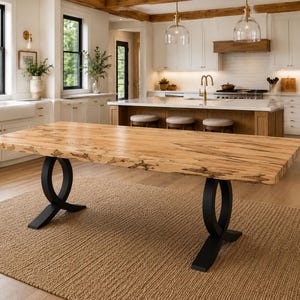 May include: A rectangular dining table featuring a natural light-colored wood slab top with visible grain and dark knots. The table is supported by two black metal bases, each consisting of a circular ring frame connected to a flat, wide base.