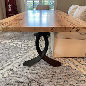 May include: A large rectangular wooden dining table with a light-colored, patterned top. The table is supported by a black, stylized metal base. The table is approximately 108 inches long.