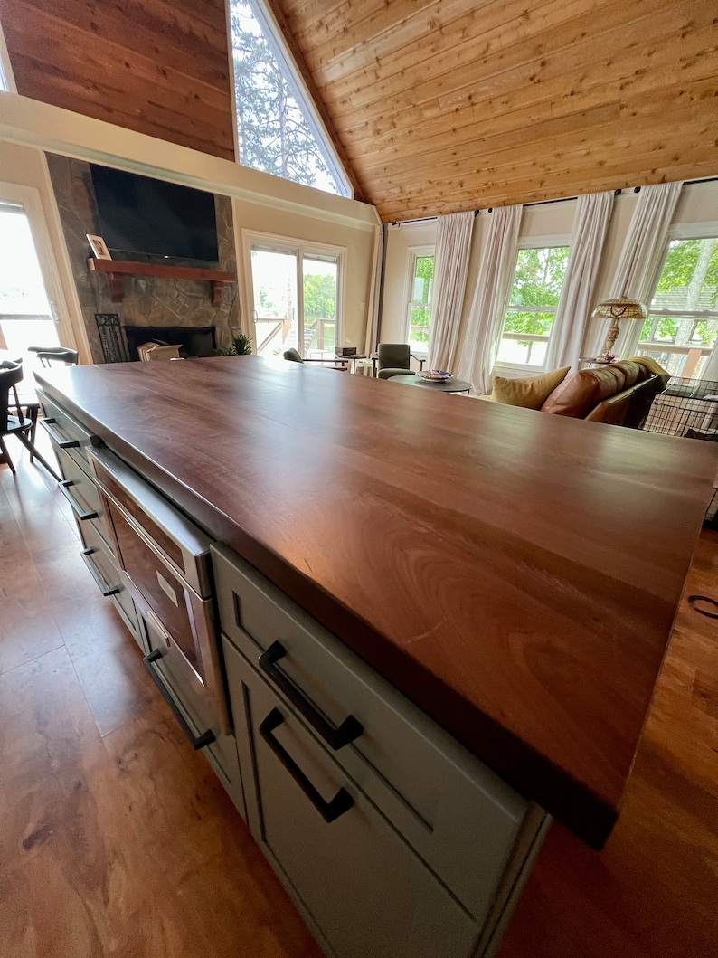 May include: A kitchen island with a light gray cabinet base and a dark wood countertop. The island has a built-in oven and two drawers with black handles.