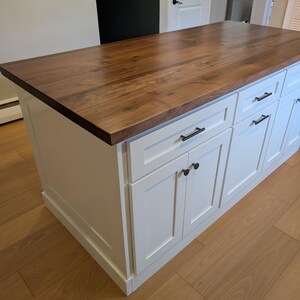 May include: White kitchen island with a wood countertop and black hardware. The island has four drawers and two doors.