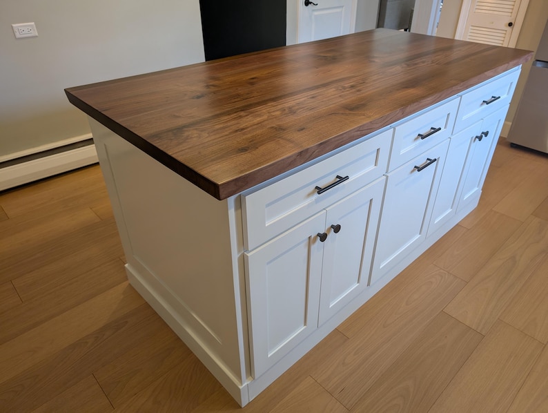 May include: White kitchen island with a wood countertop and black hardware. The island has four drawers and two doors.