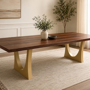 May include: A rectangular dining table with a dark brown wood grain top and two gold-colored U-shaped metal legs. The table surface is smooth and flat, featuring a natural wood texture. The base consists of two distinct, curved metal supports.