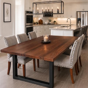 May include: A rectangular dining table with a dark brown wood grain top and a black metal U-shaped base. Six upholstered chairs with light gray fabric, nailhead trim, and dark wood legs are positioned around the table, which holds a candle.
